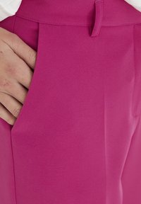 Fuksia mukautetut housut, joissa on sileä pinta, pleated-malli ja sivutaskut. Kangas näyttää olevan kevyt ja ryppyilemätön.