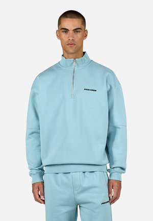 Jasnoniebieska bluza z zamkiem i ściągaczami przy mankietach oraz dolnej części, z czarnym logo "PEGADOR" na klatce piersiowej i wysokim kołnierzem.