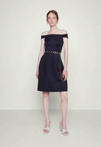 Vestido azul-marinho com decote assimétrico, corpete justo, saia rodada e detalhe de cinto de corrente dourada. Tecido liso com um brilho subtil.