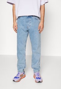 Jean bleu clair à jambes droites avec finition délavée et design à cinq poches, assorti à des chaussures de sport violettes et orange.