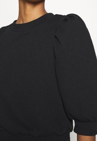 Black cotton sweatshirt featuring a rounded neckline, puff sleeves, and a fitted hem. Texture is smooth with a soft, casual design.