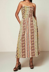 Robe longue bustier présentant un motif multicolore avec des rayures verticales vertes, marron et orange, dotée de poches latérales et d'un corsage ajusté.