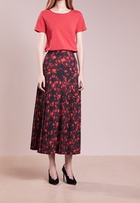Maglietta rossa a maniche corte abbinata a una lunga gonna nera plissettata con un motivo floreale rosso. Scarpe nere con tacco alto completano l'outfit.