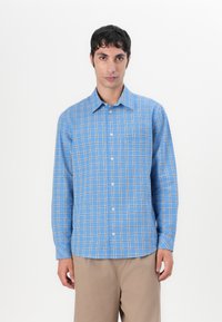Hellblau kariertes Button-up-Hemd mit langen Ärmeln, das eine Brusttasche und einen abgerundeten Saum hat. Hergestellt aus weichem Baumwollstoff.