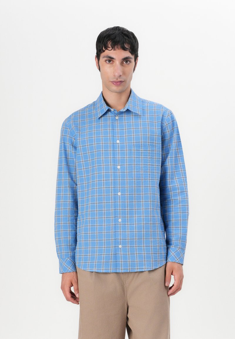 Hellblau kariertes Button-up-Hemd mit langen Ärmeln, das eine Brusttasche und einen abgerundeten Saum hat. Hergestellt aus weichem Baumwollstoff.
