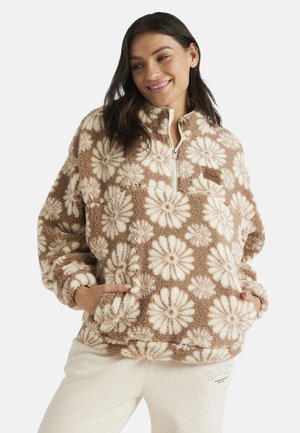 Fuzzy brown fleece pullover with white daisy pattern, half-zipper, and side pockets. Features a logo patch on the chest.
