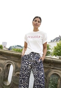 Bílá trička s červeným nápisem "POSITIVE", spárované s širokými kalhotami s leopardím vzorem. Hladká tkanina, volný střih a srolované rukávy.