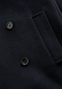 Abrigo de lana azul marino con diseño de doble botonadura, textura suave, dos botones negros y un bolsillo en el pecho.