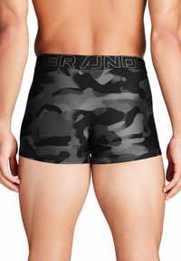 Svart kameleontmönstrad herrunderkläder med en texturerad midjeband märkt "Under Armour." Har en åtsittande passform och kort bendesign.