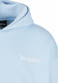 Sweat à capuche bleu clair avec capuche pliée et texte brodé blanc "Dropsize" sur la poitrine, montrant une partie de l'épaule gauche.