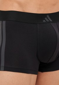 Boxer shorts pretos para homens, com uma faixa elástica preta apresentando um logotipo cinza. Textura suave, design ajustado e riscas laterais contrastantes.