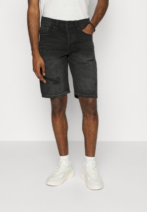 Schwarze Jeansshorts mit verwaschenem Design, mittlerer Länge, Fünf-Taschen-Stil und klassischem Bund. Kombiniert mit weißen Turnschuhen.