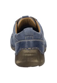 Chaussure en cuir bleu avec un talon arrondi, des coutures décoratives et une texture lisse. L'intérieur est beige, contrastant avec la couleur extérieure.