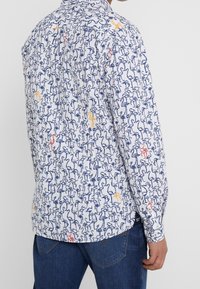 Camicia bianca a maniche lunghe con un stampa di uccelli colorata in blu, rosso e giallo, collo a bottoni e vestibilità comoda.