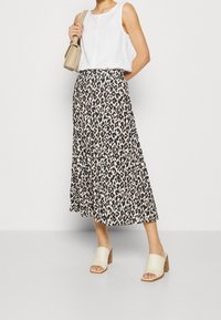 Jupe midi imprimé léopard, tissu léger, coupe évasée, tons noir et beige. Associée à un débardeur blanc et des mules à bout fermé.