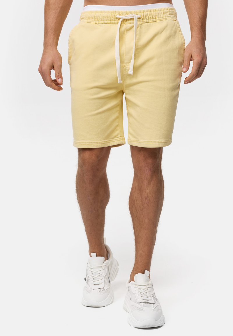 Shorts en coton jaunes avec une taille élastique et un cordon de serrage. Poches latérales et coupe décontractée. Assortis à des chaussures de sport blanches.