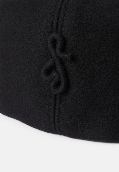 Musta villahattu, jossa on teksturoitu pinta, hienovaraiset ommel yksityiskohdat ja sivulla oleva silmukka. Pyöreä muoto, keskikorkeus.
