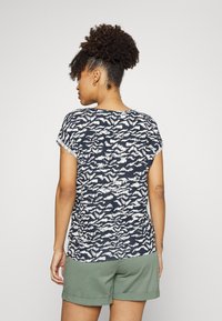 T-shirt azul-marinho com padrão abstrato branco, mangas curtas, corte descontraído, tecido suave; combinado com calções verdes, com as bainhas arrolhadas.