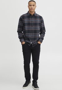 Czarna i granatowa koszula w kratę z klasycznym kołnierzykiem, w połączeniu z czarnymi, slim fit spodniami i czarnymi trampkami z białą podeszwą.