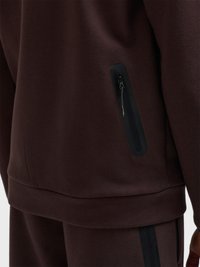 Nahaufnahme von dunkelbrauner Kleidung mit einer vertikalen schwarzen Reißverschlusstasche an der Seite einer Jacke oder eines Sweatshirts.