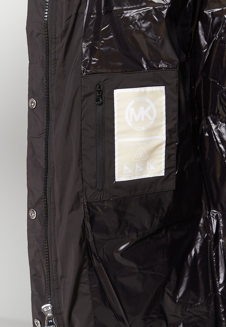 Schwarze Steppjacke innen mit einer Reißverschlusstasche, einem Stoffetikett mit Markenlogo und einer glänzenden, glatten Oberfläche.