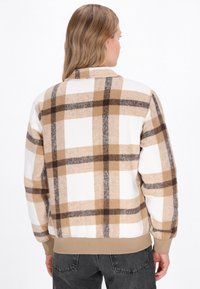 Ruudullinen takki, jossa on kerma-, ruskea- ja vaaleanruskea sävy, valmistettu fleece-materiaalista, jossa on ribattu helma ja hihansuut; sisältää rento siluetti ja kaulus.