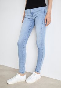 Jean ajustados de un azul claro hechos de denim, con una cintura a media altura y detalles de costura mínimos, combinados con zapatillas blancas.