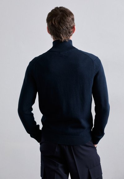 Temno modra pletena pulover s visokim ovratnikom, rebrastimi manšetami in spodnjim delom; ima brezšivno zasnovo ramen in fino teksturo.
