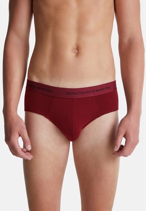 Mannelijke torso met maroon boxershort en een tailleband met het merk "United Colors of Benetton" op een witte achtergrond.