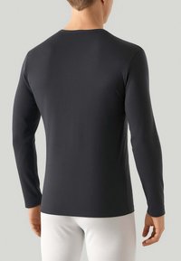 Camicia a maniche lunghe in tessuto grigio scuro, con scollatura a girocollo e design aderente, caratterizzata da una texture liscia e cuciture minime, indossata con pantaloni bianchi.