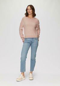 Lichtroze gebreide trui met een ronde hals en een relaxte pasvorm, gecombineerd met lichtblauwe straight-leg jeans en beige plateausneakers.