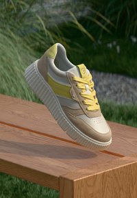 Baskets avec une palette de couleurs beige et jaune clair, en matériaux en daim et synthétiques, avec une semelle blanche épaisse et des détails de laçage marquants.