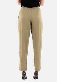 Pantaloni khaki a sigaretta con vita elastica e polsini, caratterizzati da una texture liscia e un drappeggio sottile, abbinati a scarpe nere con tacco alto.