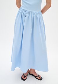 Jupe bleu clair, longueur cheville, en tissu doux avec une taille froncée et deux poches latérales, assortie à des tongs noires.