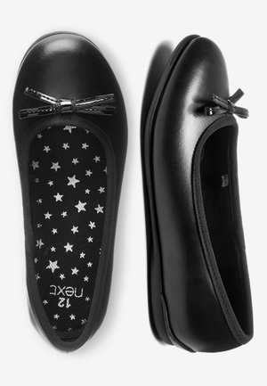 Paar schwarze glänzende Ballerinas mit kleinen Schleifen an den Zehen und sternenmusterte Innensohlen, auf weißem Hintergrund präsentiert.