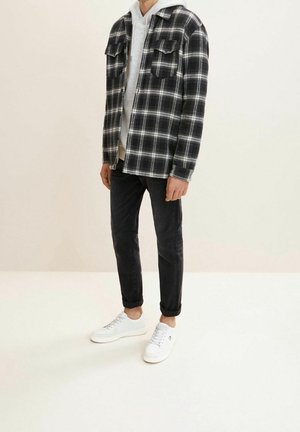 Koszula w kratę w czerni i bieli, nałożona na jasnoszary hoodie. Para ciemnych dżinsów i białe trampki dopełniają outfit.