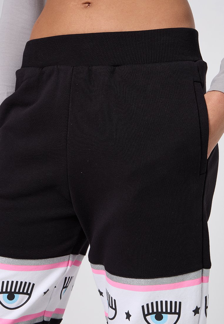 Schwarze Hose mit einem gerippten Bund, der im unteren Bereich mit einem grafischen Augendesign und rosa sowie metallischen silbernen Akzenten verziert ist.