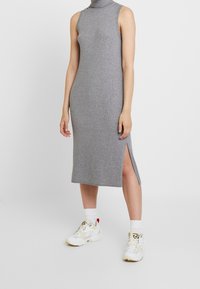 Grå ribbad stickad ärmlös klänning med hög hals och en sidofiss, matchad med vita sneakers och vita strumpor.