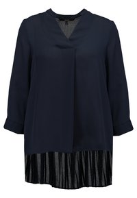 Blusa a maniche lunghe blu navy con scollo a V, design a strati, con un sottogonna in tulle nero plissettato all'orlo. Tessuto morbido con leggera lucentezza.