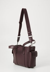 Tamsiai burgundi  odinė rankinė su tekstūruotu audinio dirželiu. Pasižymi keliais kišenėmis ir elegantišku siuvinėjimu. Kompaktiško kvadratinio formato.