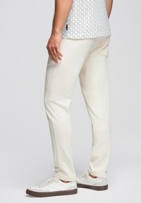 Weiße Baumwollmischungshose mit schlankem Schnitt, versehen mit Seitentaschen und glatter Textur. Kombiniert mit weißen Sneakers und einem gemusterten Oberteil.