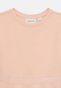 T-shirt de algodão rosa da Calvin Klein com gola redonda, mangas curtas e um destaque em logo branco na parte inferior. Textura suave e macia.