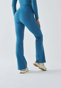 Niebieskie spodnie sportowe o rozszerzanych nogawkach wykonane z elastycznej tkaniny, charakteryzujące się gładką fakturą i średnio wysokim stanem, zestawione z jasnobeżowymi tenisówkami.