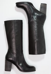 Bottes hautes noires en cuir jusqu'aux genoux avec un talon bloc large et côtelé. Texture lisse avec une silhouette épurée et des détails de coutures minimalistes.