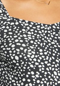 Tecido preto com manchas brancas irregulares, com decote quadrado e superfície texturizada. Um colar simples dourado realça o design.