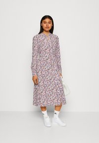 Robe midi florale avec manches longues, col à revers et jupe à volants. Présente un imprimé de fleurs violettes, roses et bleues sur un fond blanc.