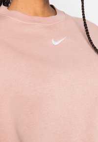 Ljusrosa sweatshirt med rund halsringning och ribbade muddar. Har en liten vit Nike-logga på övre vänstra sidan. Mjuk, bomullsmaterial.