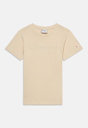 T-shirt beige à manches courtes de la marque Champion avec logo en relief sur la poitrine et petite étiquette logo sur la manche gauche.