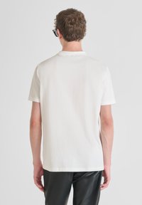 Camiseta blanca de manga corta con una textura suave y un escote redondo, combinada con pantalones negros brillantes. Diseño minimalista, sin patrones visibles.