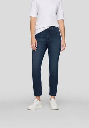 Dark blue denim jeans with a fitted design, mid-rise waist, and subtle stitching details, paired with white sneakers and a short-sleeve white top.